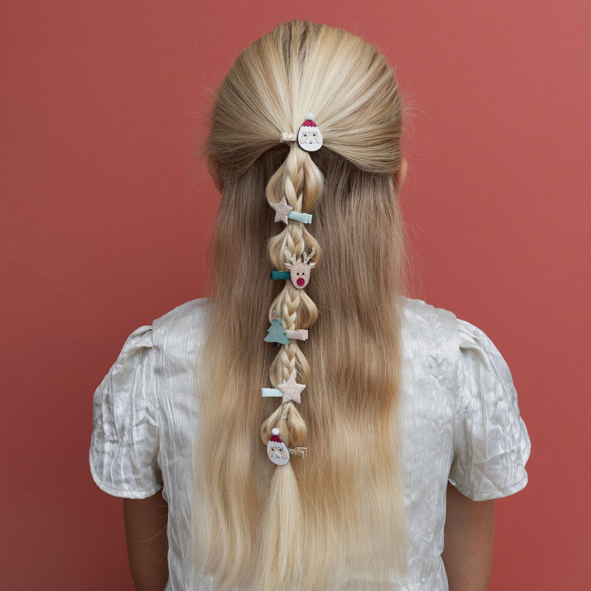 Person with long blonde hair styled in braids with decorative hair clips against a red background