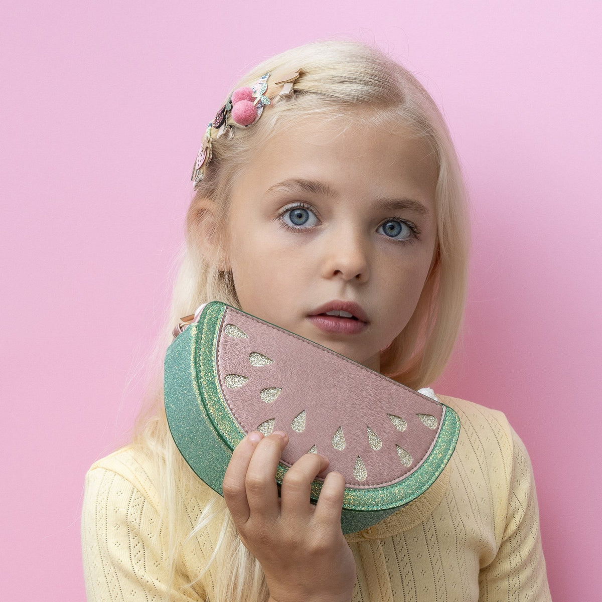 Young girl holding a watermelon-shaped clutch against a pink background