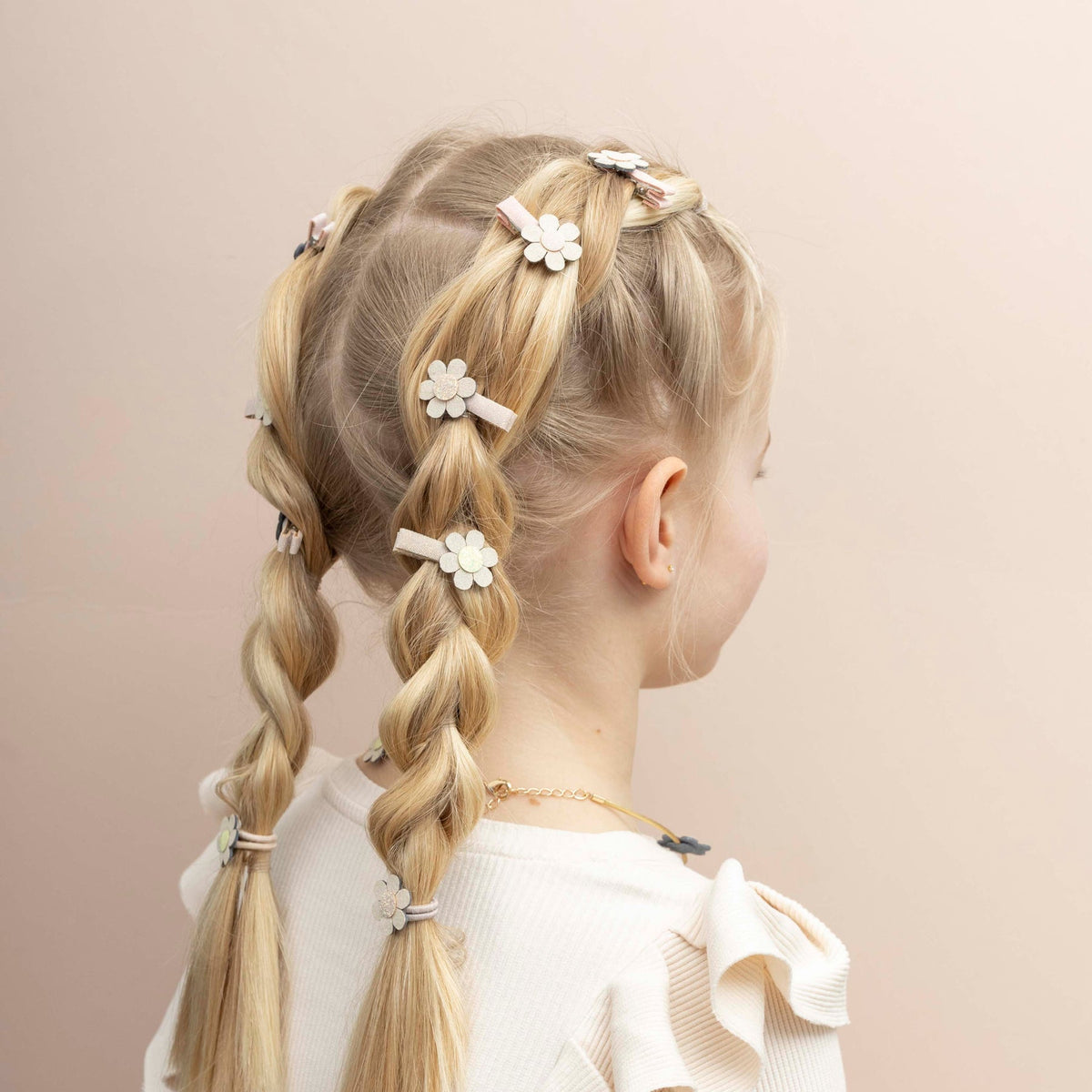 Child with braided hair adorned with floral hair clips on a beige background