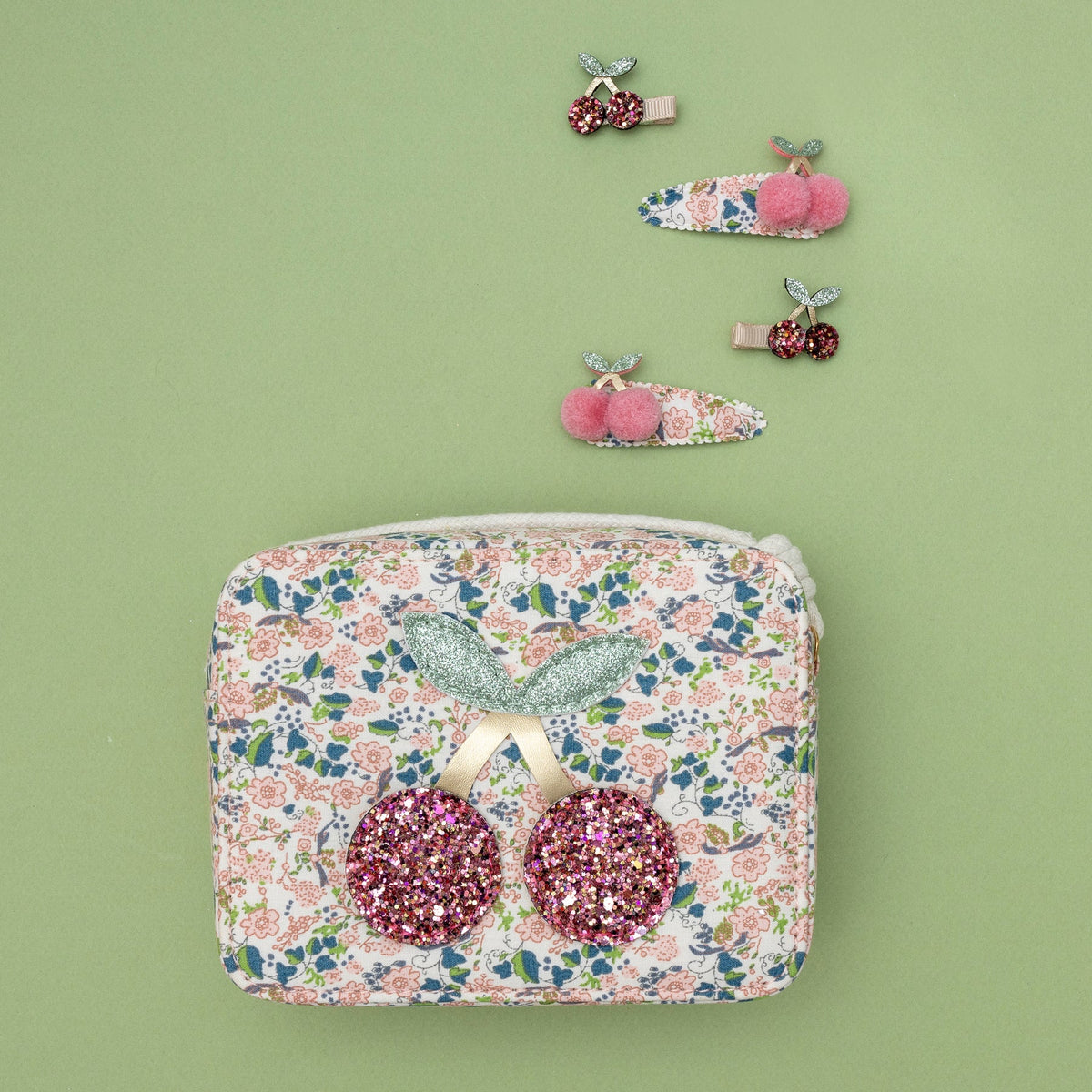 Floral patterned pouch with pink glittery earrings and decorative hair clips on a green background