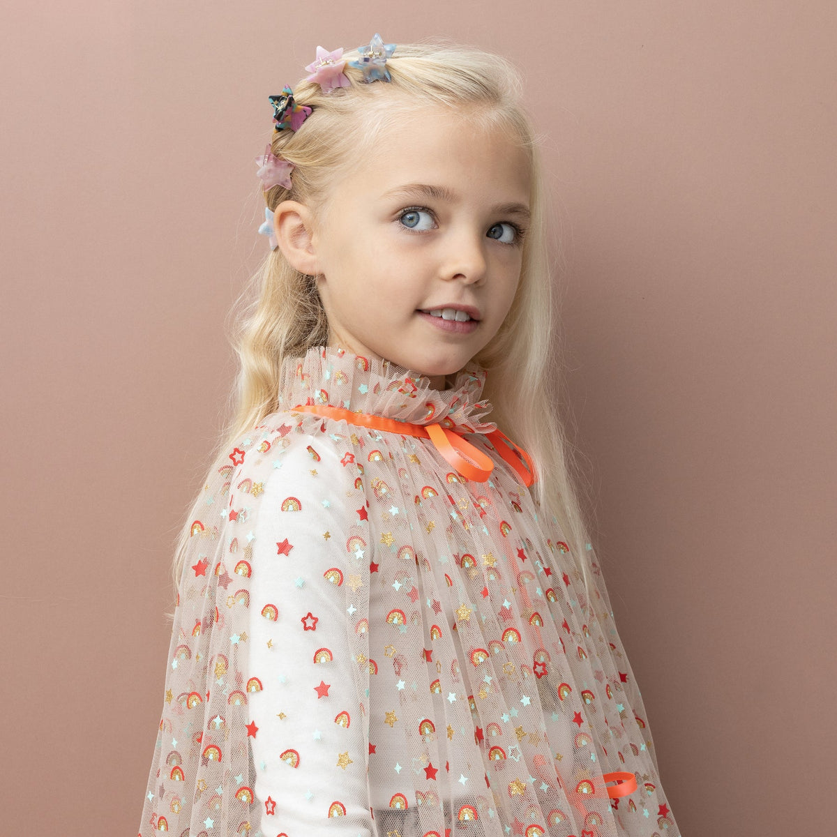 Young girl with blonde hair and blue eyes against a pink background