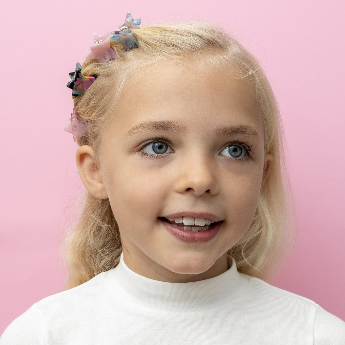 Young girl with blonde hair and blue eyes against a pink background