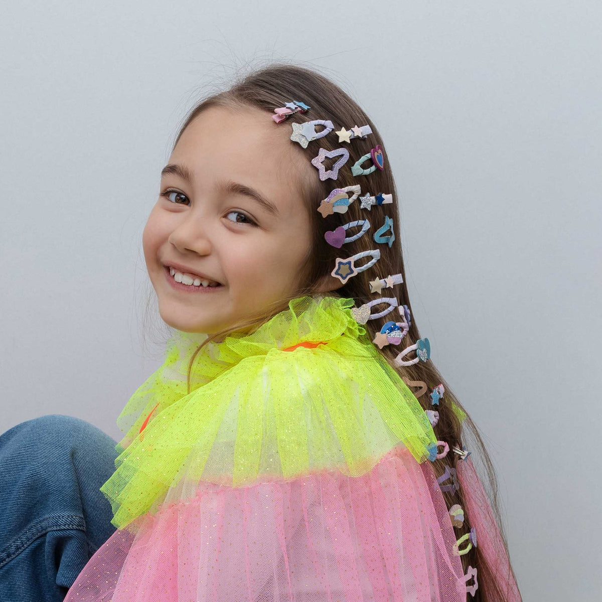 Young girl with colorful hair clips in her hair against a plain background