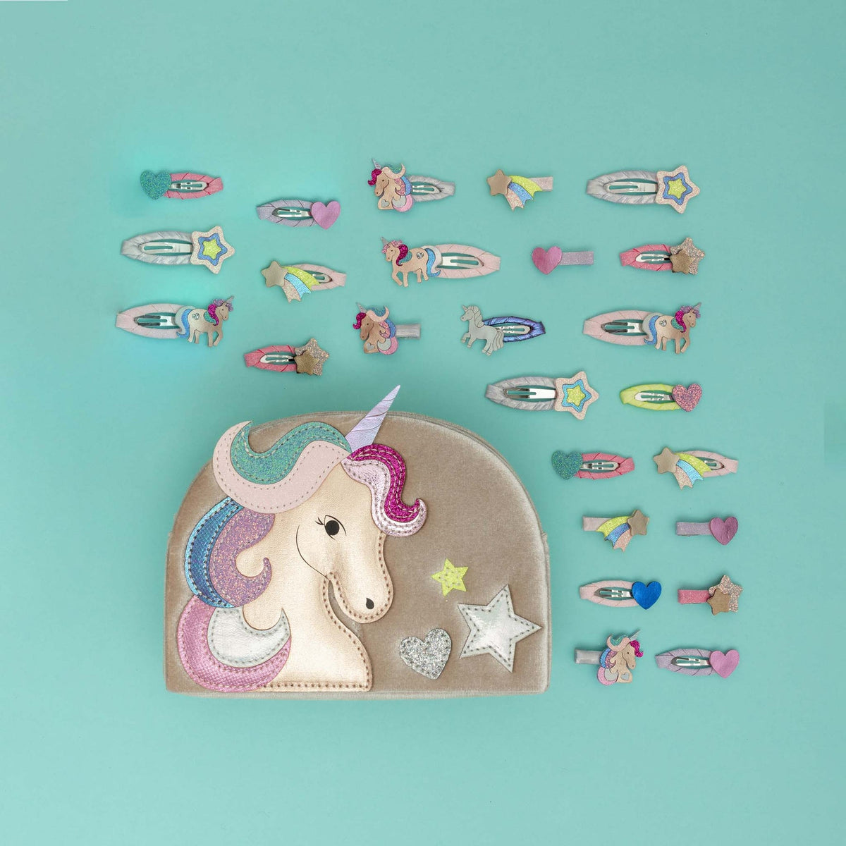A pastel unicorn-themed hair accessory set arranged on a light aqua background, featuring a large fabric pouch with an embroidered unicorn head and a row of matching hair clips and pins in unicorn, star, and rainbow designs.