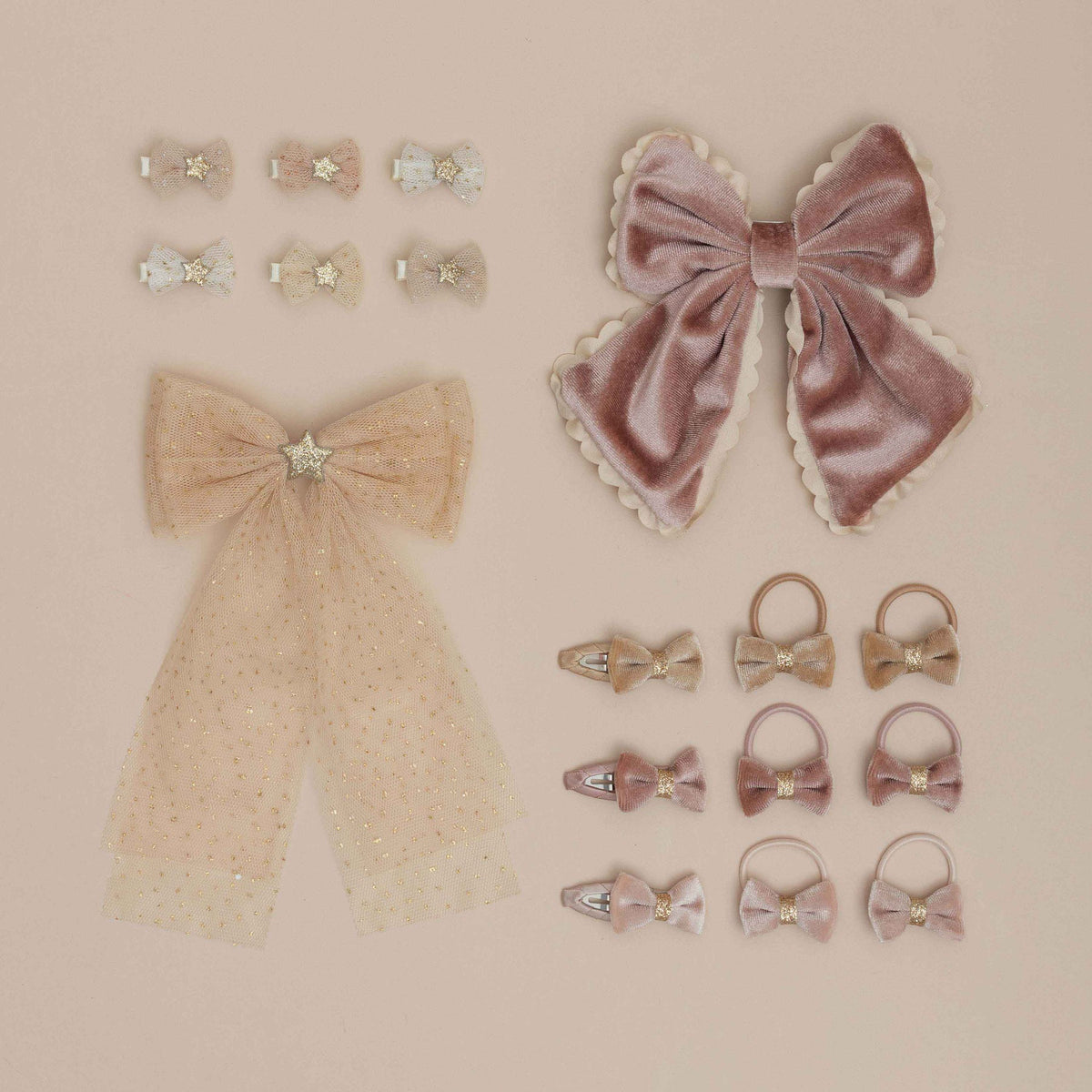 A set of pastel hair accessories arranged on a warm beige background, including two large bow clips, several small bow hair clips, and multiple hair ties in dusty pink, champagne, and cream tones with rhinestone accents.