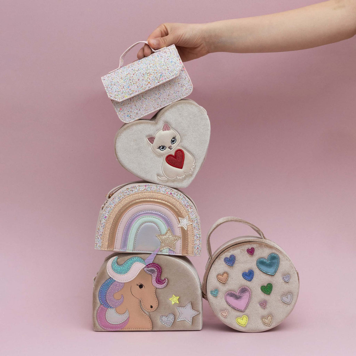 Stack of colorful children's bags with a hand holding the top one against a pink background