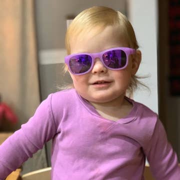 Child wearing purple sunglasses and a matching outfit indoors.