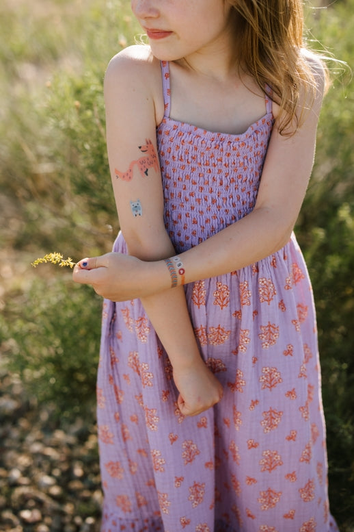 Young girl in a floral dress holding a small plant in a natural setting