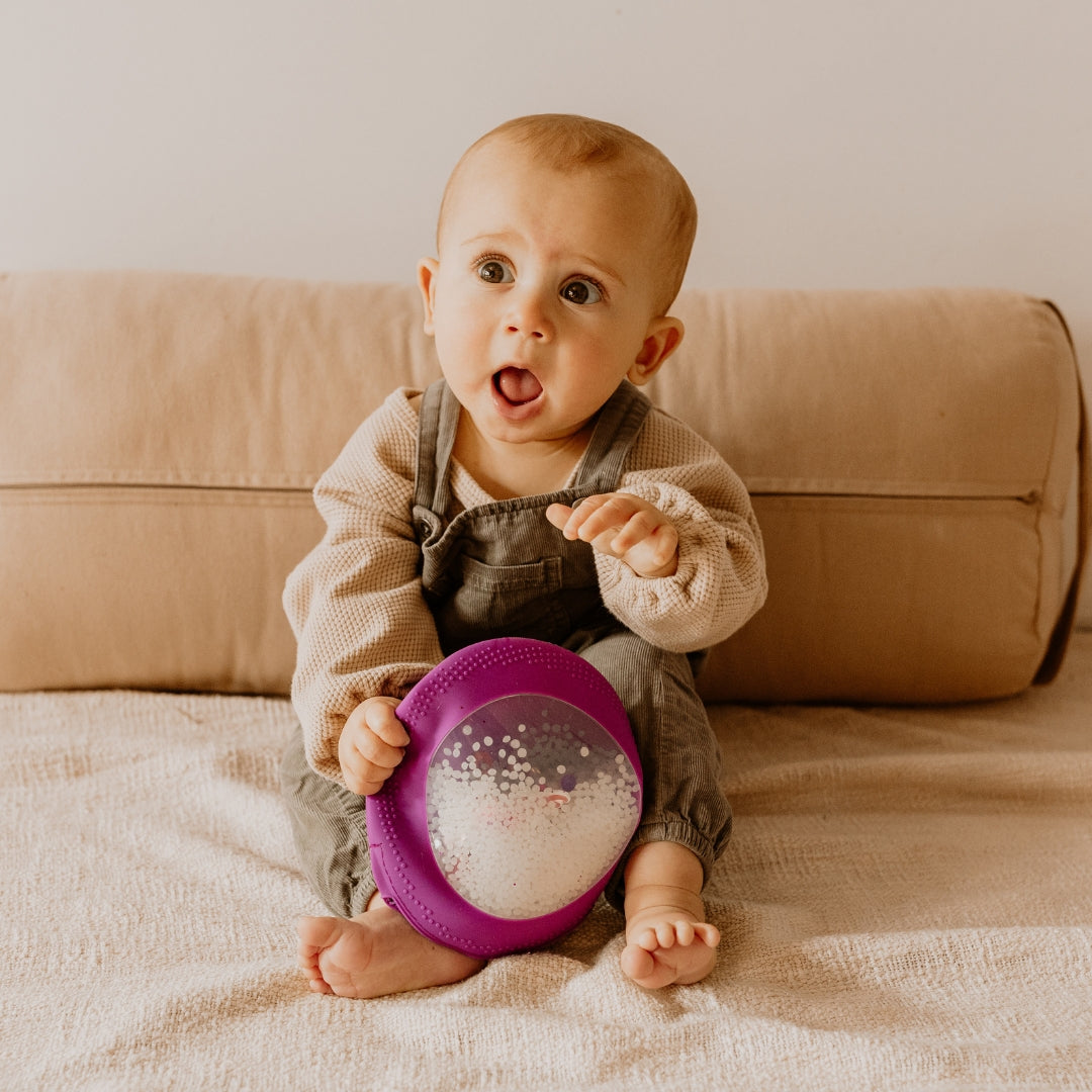 Baby sitting on a couch holding a purple toy