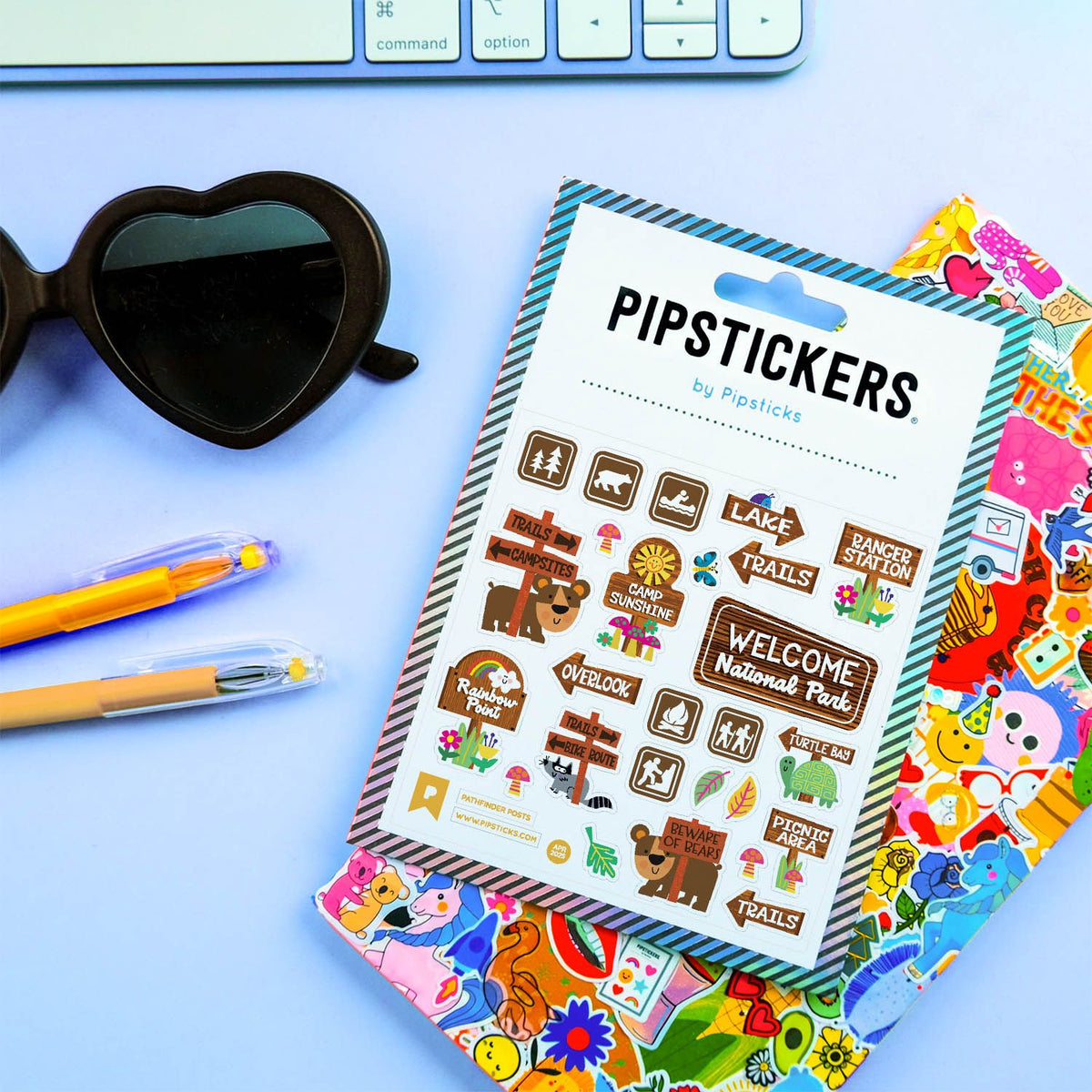 Packaged PipStickers with colorful designs on a blue surface with sunglasses and pens.