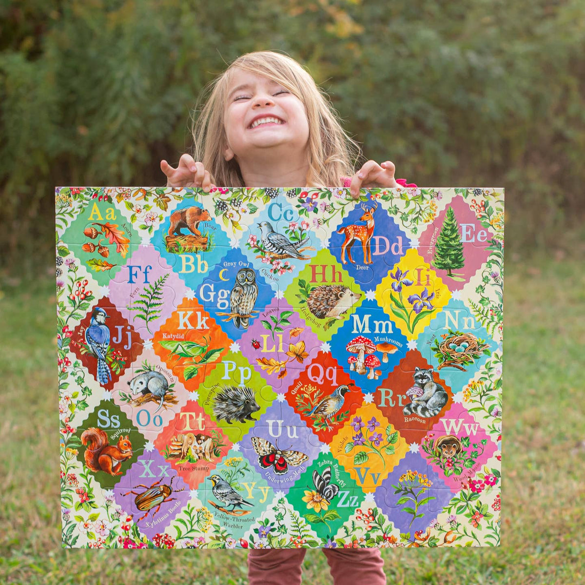 Child holding a colorful alphabet poster outdoors