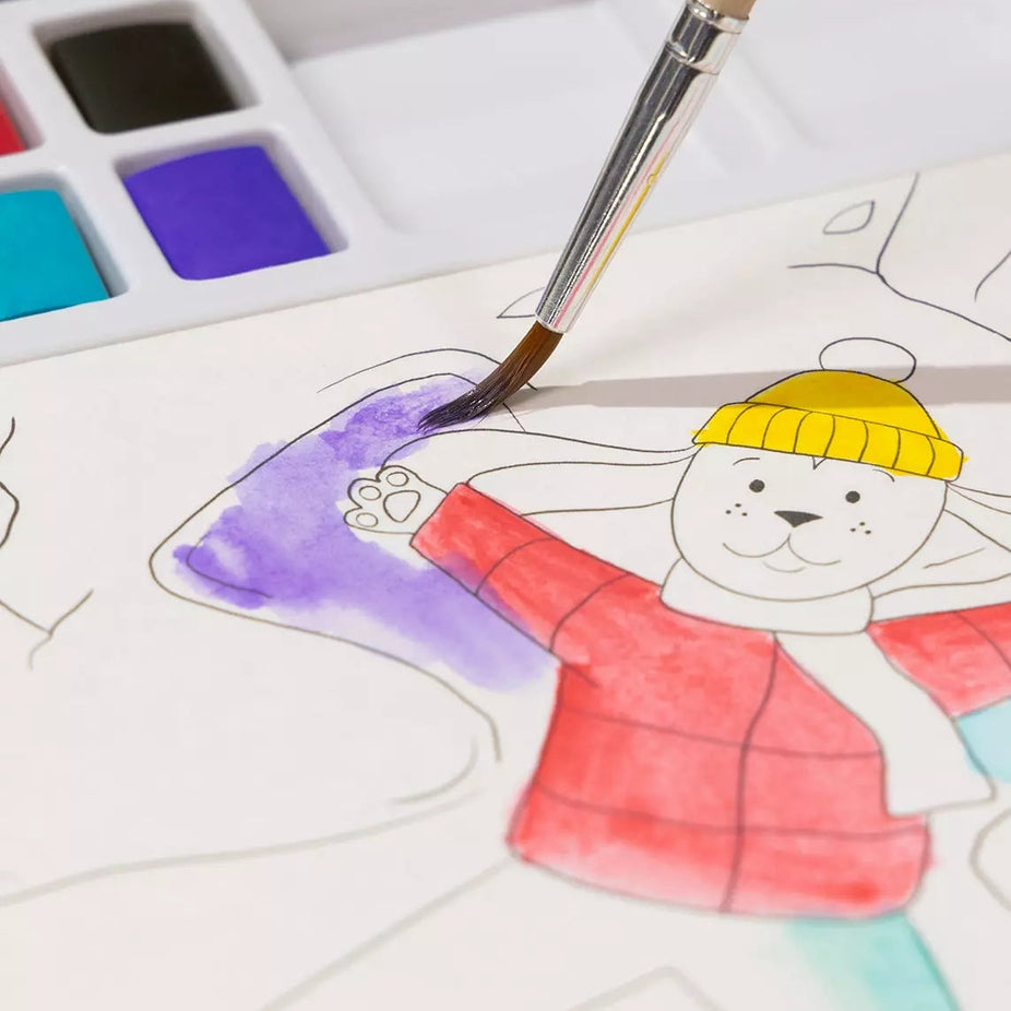 A close-up of a child's watercolor painting in progress, showing a cartoon bear character being painted with a paintbrush. The bear is wearing a yellow beanie and a red jacket, with purple and teal colors being applied.