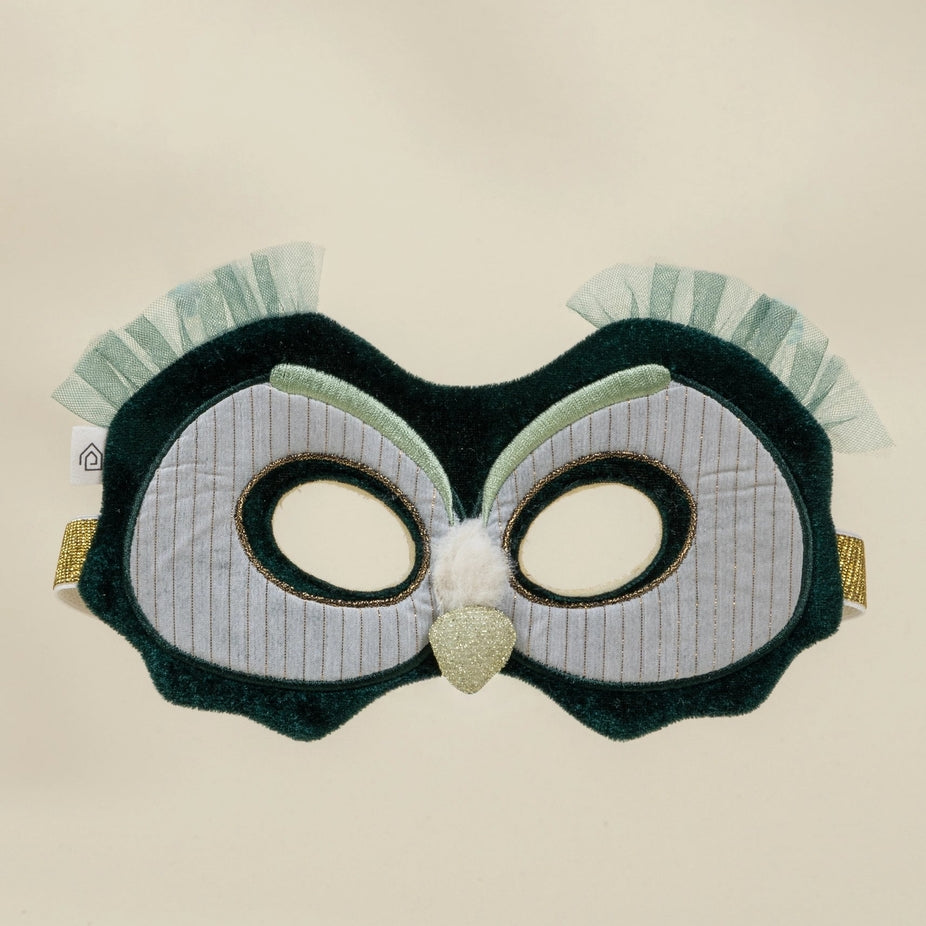 An owl-themed costume mask featuring a dark green plush body, white pinstriped eye panels, a glittery gold beak, and light green ruffled feathers on the sides, shown against a plain beige background.