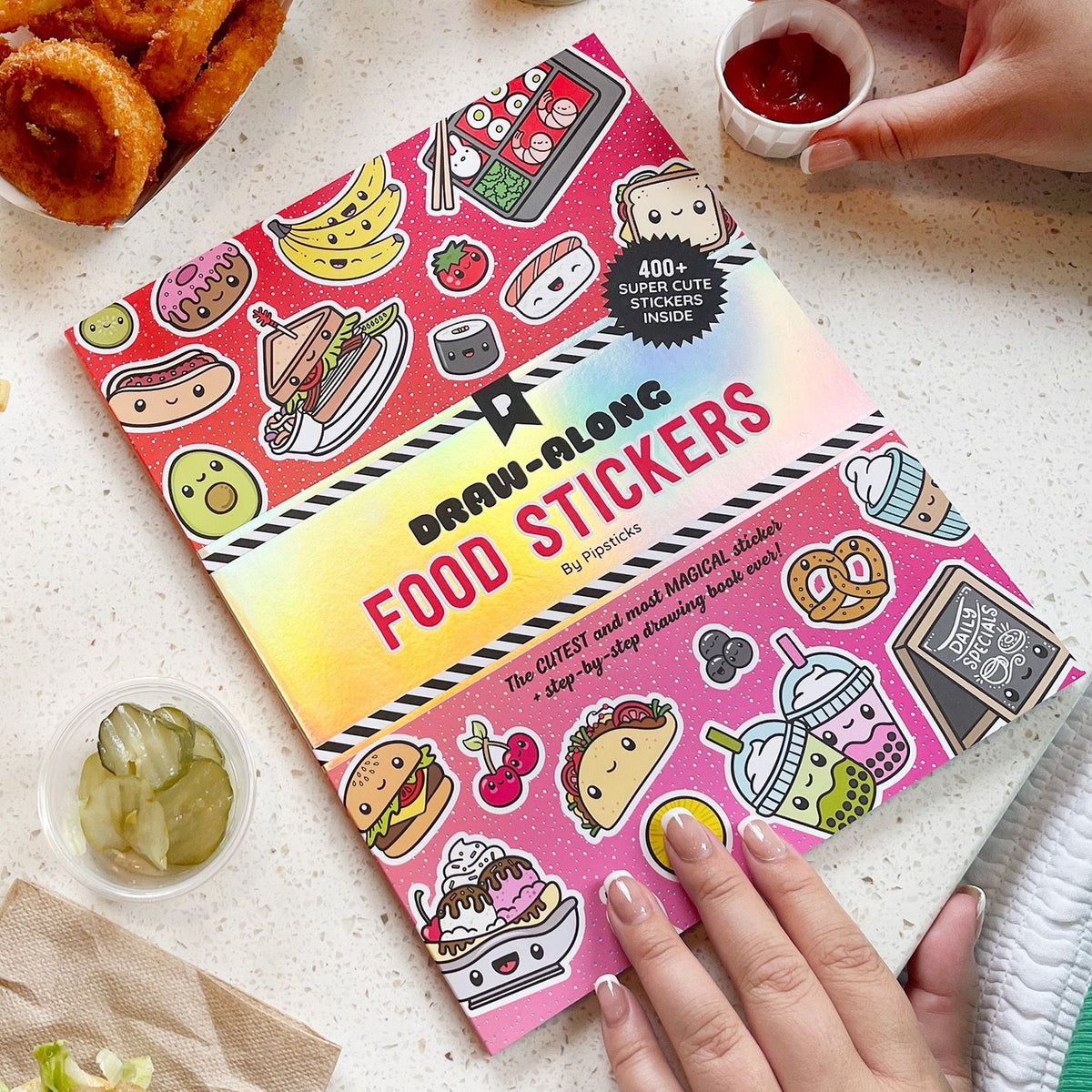 Food-themed draw-along stickers book on a table with snacks.