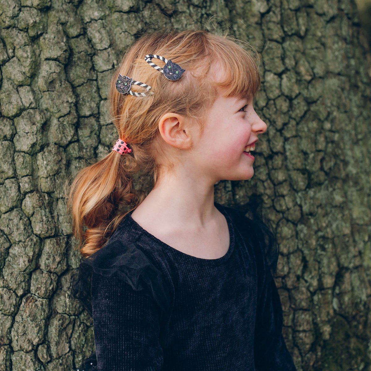 Young girl with hair clips standing against a tree trunk