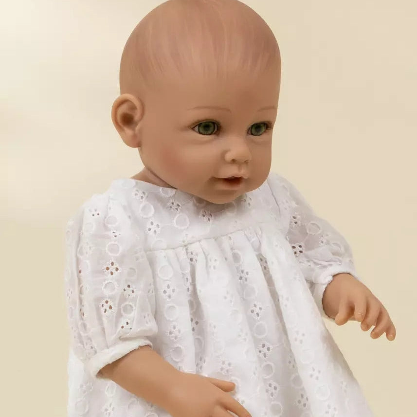 Baby doll wearing a white dress against a beige background