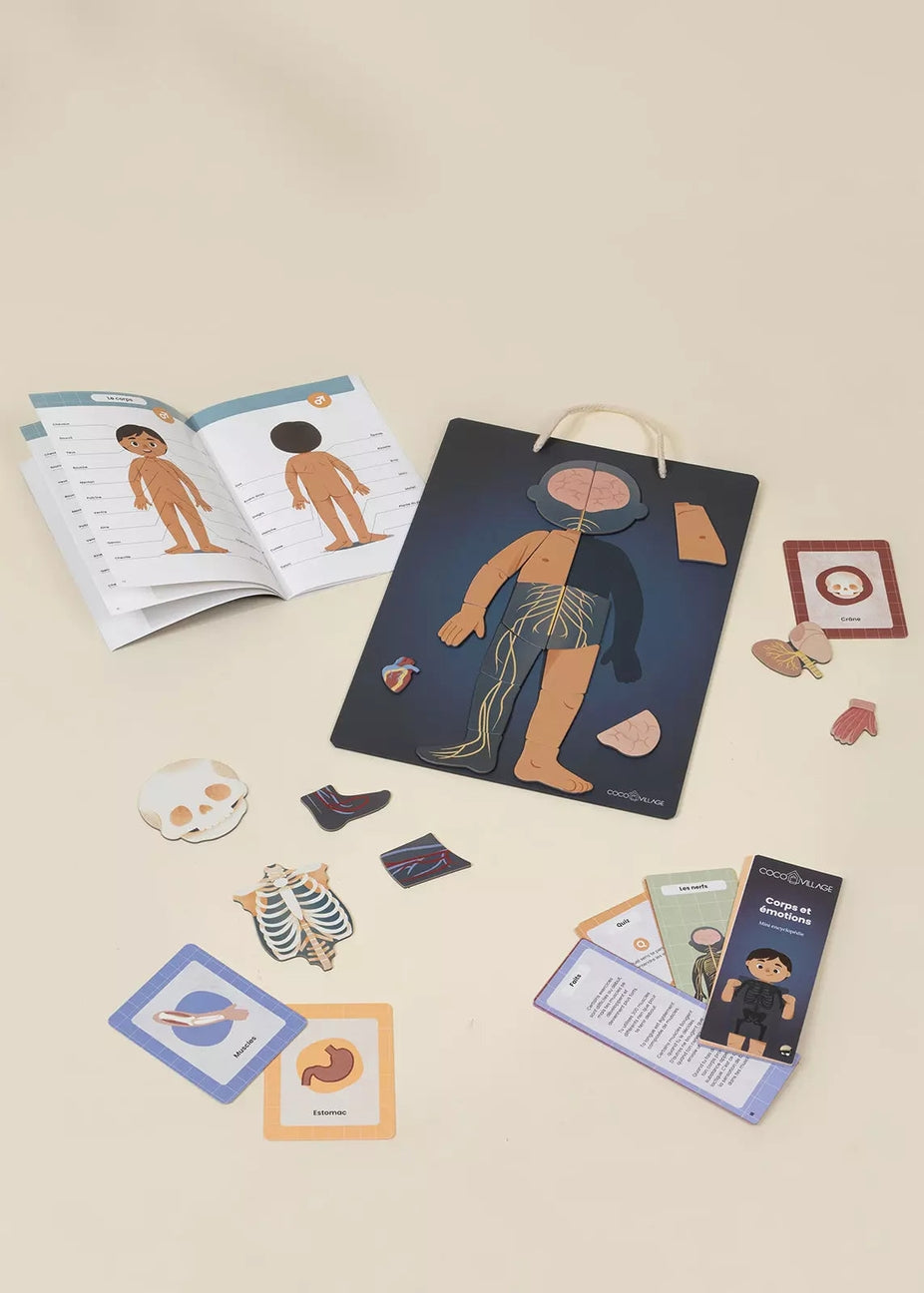 An educational medical play set arranged on a light beige background, featuring a dark blue storage bag with anatomical cutouts, an open instruction booklet, multiple colored instruction cards, and small wooden medical-themed pieces.