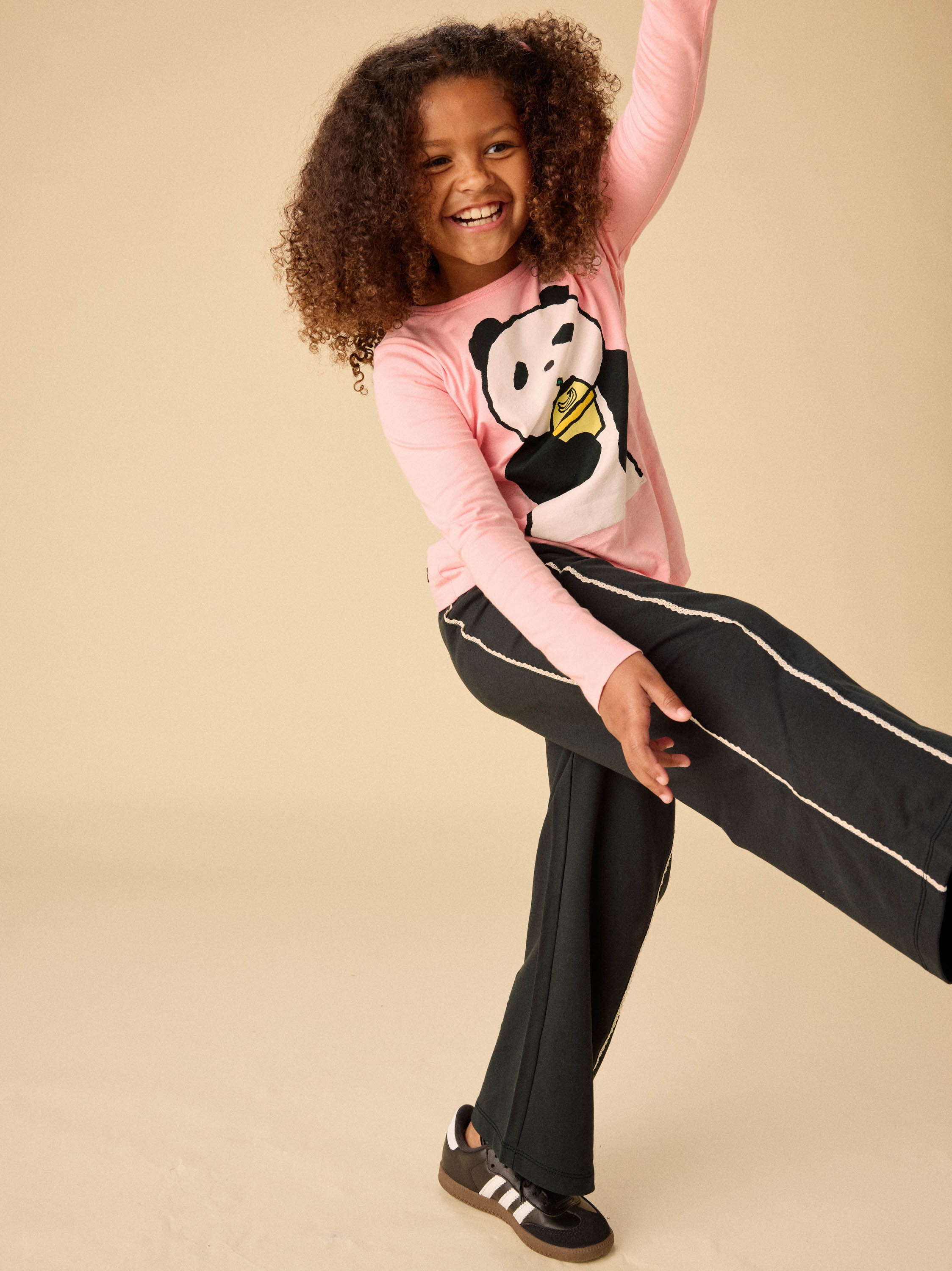 Child wearing a pink sweater with a panda design and black pants on a beige background