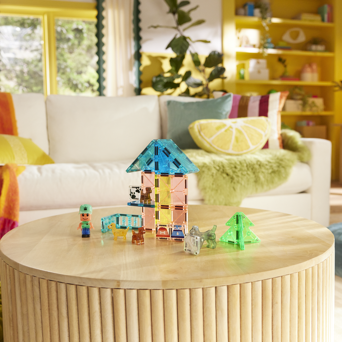 Children's playroom with colorful toys on a wooden coffee table, white sofa with cushions, and yellow walls.