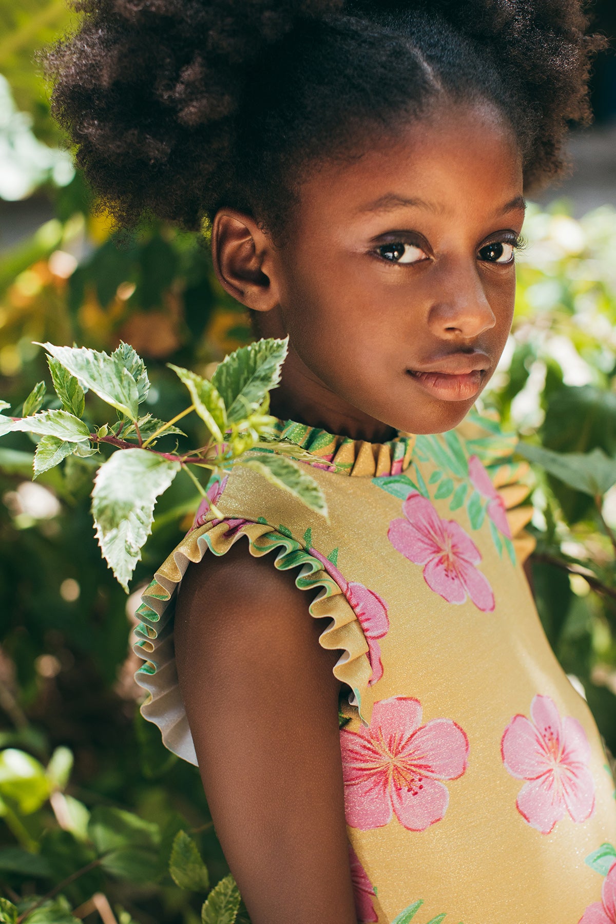 Young girl in a floral dress standing among green foliage