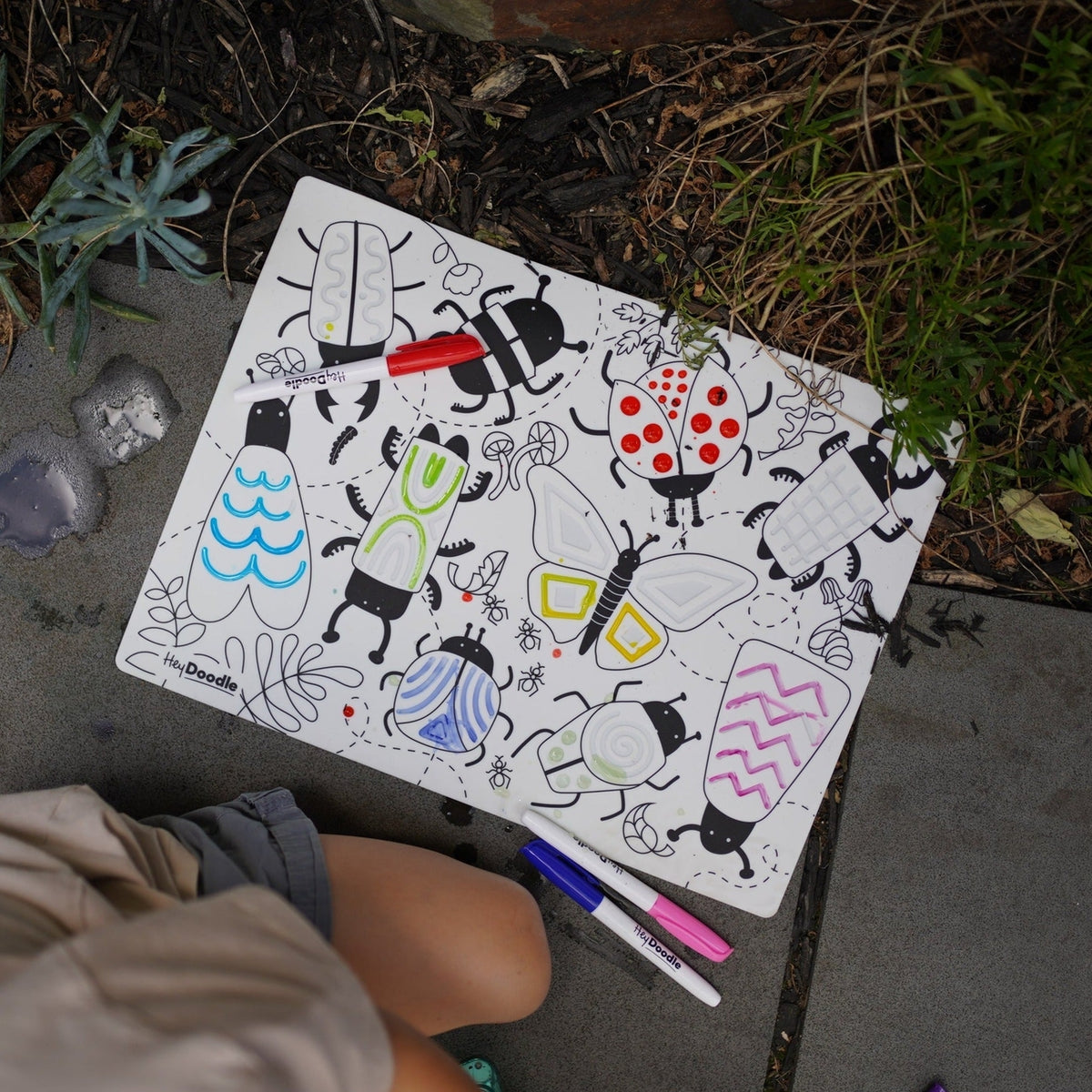 Coloring book with insect illustrations and markers on a concrete surface.