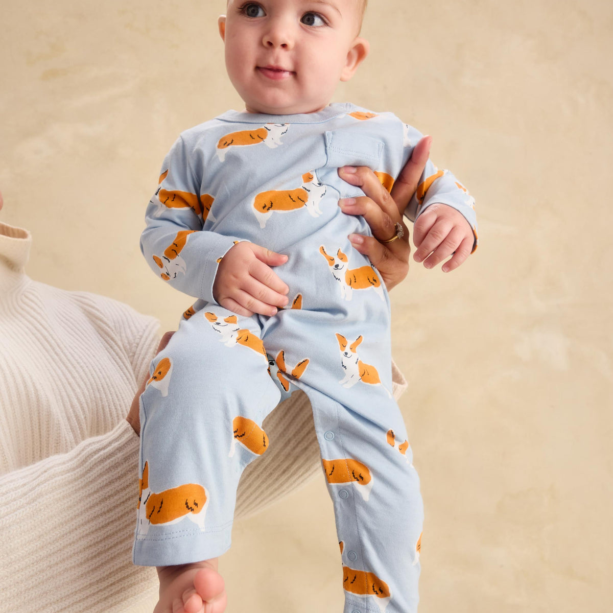 A baby wearing a light blue long-sleeve pajama set with an orange and white rabbit print, held by an adult against a warm beige background.