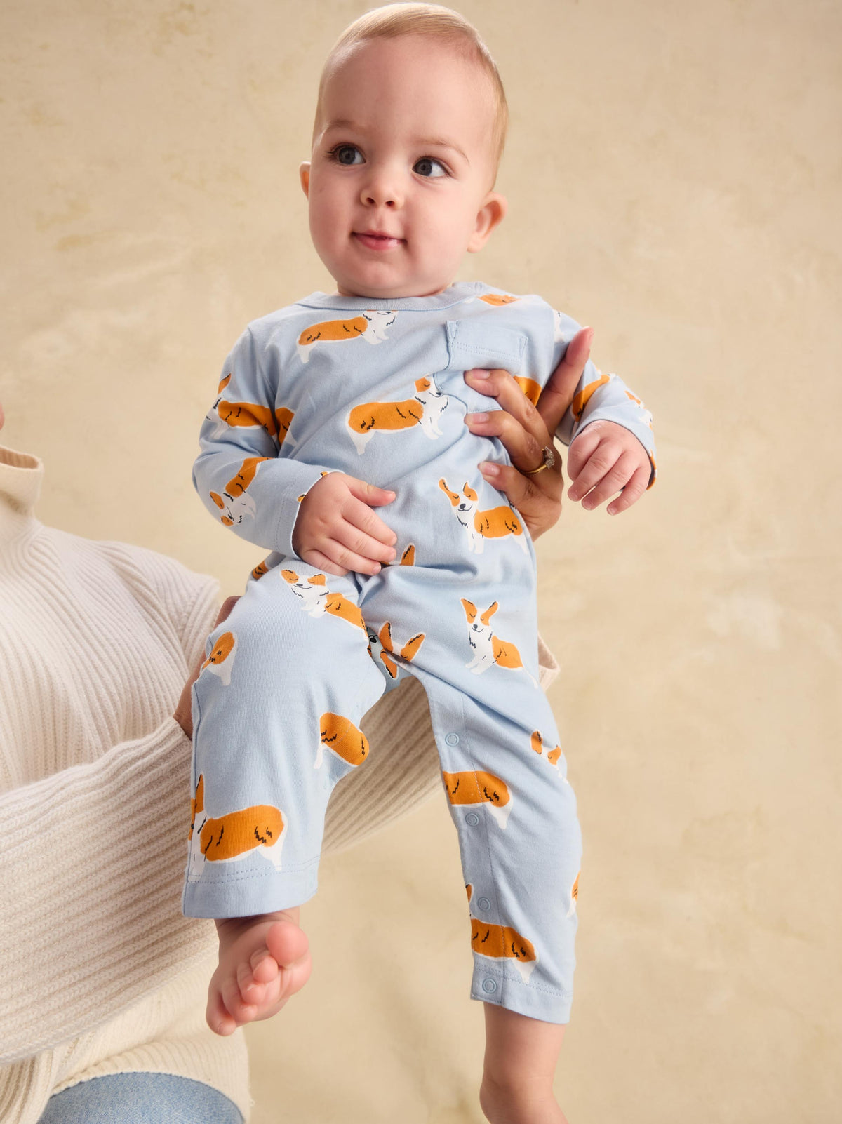 A baby wearing a light blue long-sleeve pajama set with an orange and white rabbit print, held by an adult against a warm beige background.