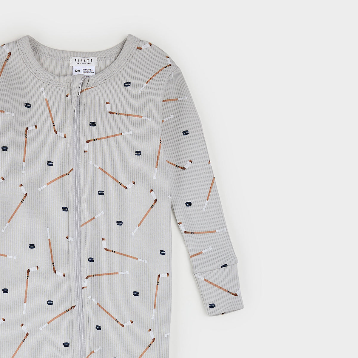 A baby long-sleeve zip-up romper in light gray ribbed fabric, featuring an all-over print of hockey pucks and sticks in brown, white, and navy blue. The brand name 'FINISK' is visible on the inner neck label.