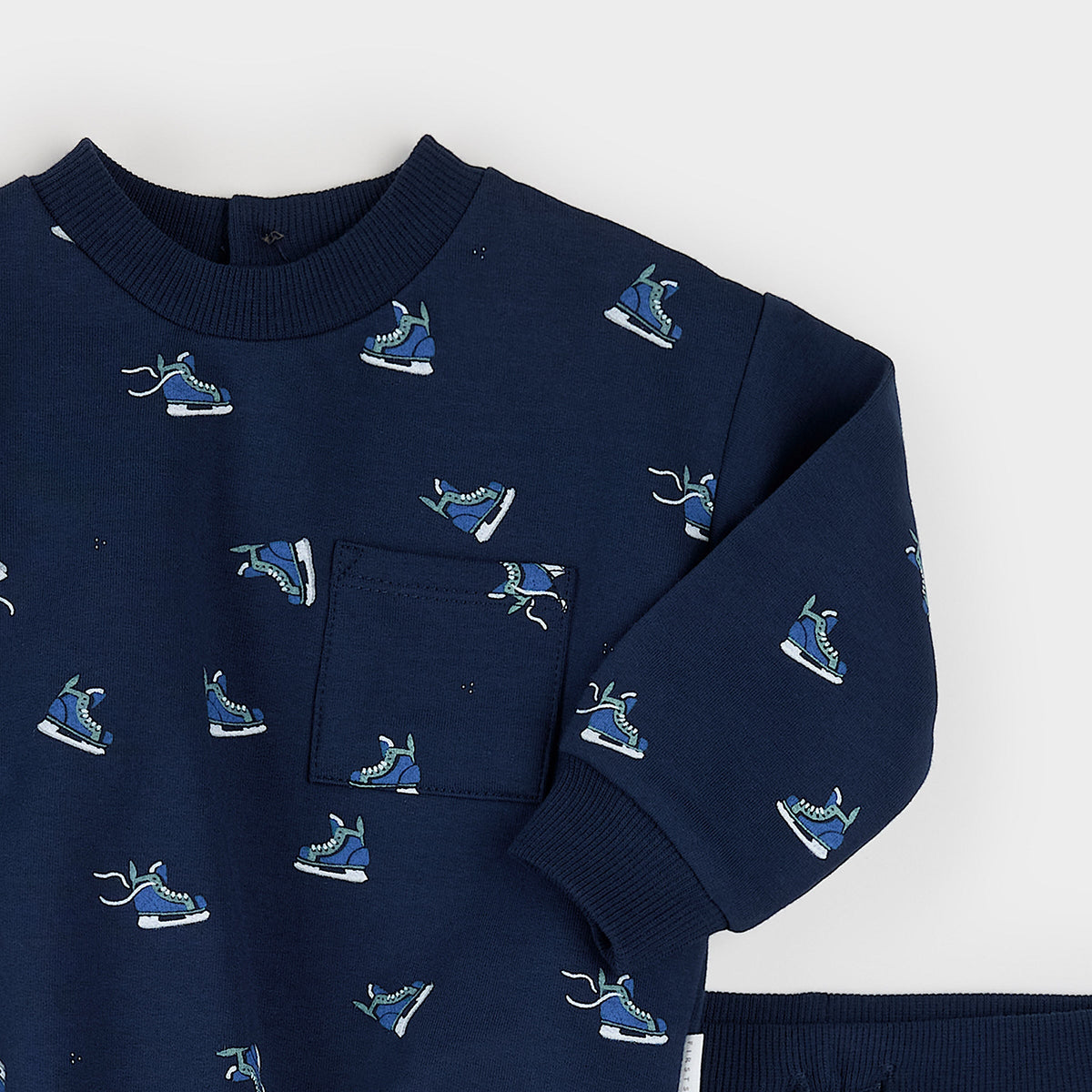 A navy blue long-sleeve sweatshirt with an all-over pattern of blue and white ice skates, featuring a ribbed crew neck and a chest pocket, shown on a light gray background.