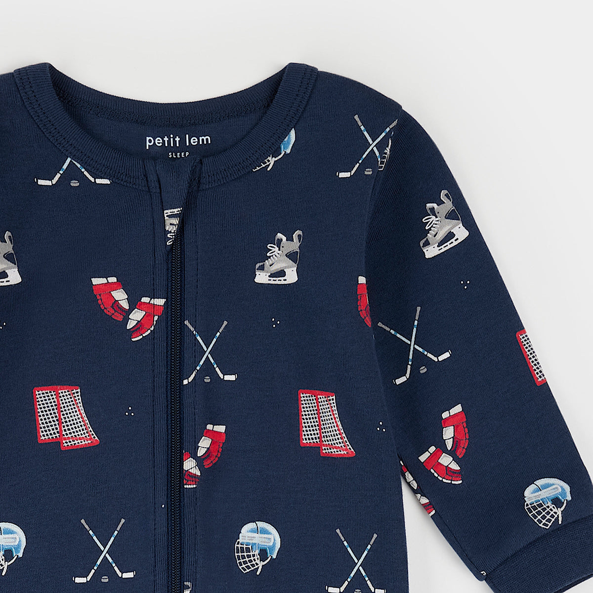 Close-up a navy blue baby footed sleeper with a front zipper and an all-over print of hockey-themed graphics including crossed sticks, helmets, skates, and the word 'BOSTON' in red.