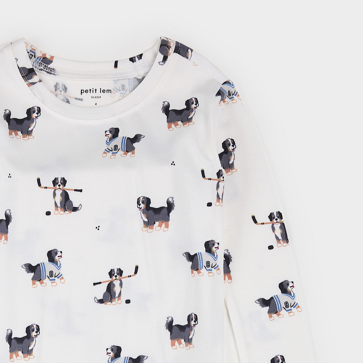 A close-up of a white long-sleeve top by petit lem, featuring an all-over print of Bernese Mountain Dogs playing hockey.