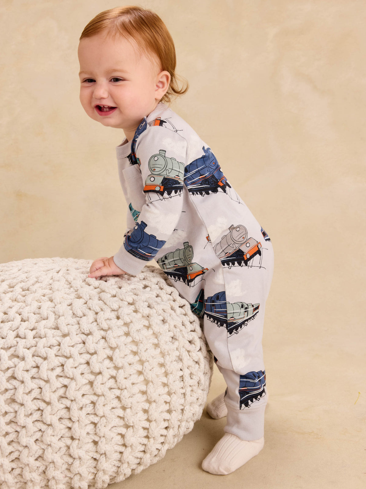 Baby crawling in a long sleeve romper with an all-over vintage steam locomotive train print, viewed from the side.