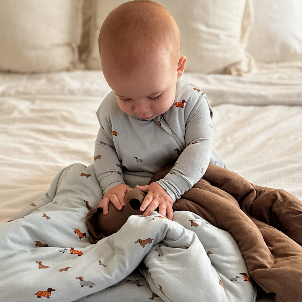 Baby sitting on a bed with a gray blanket and brown pants