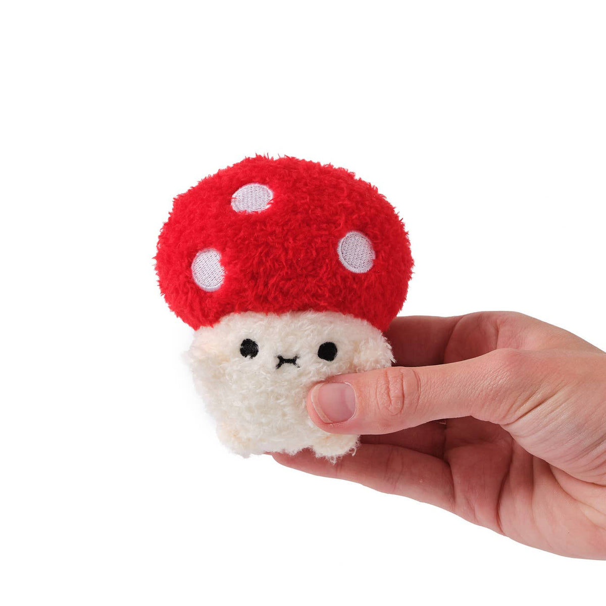 Small plush toy resembling a red mushroom with white spots held in a hand against a white background