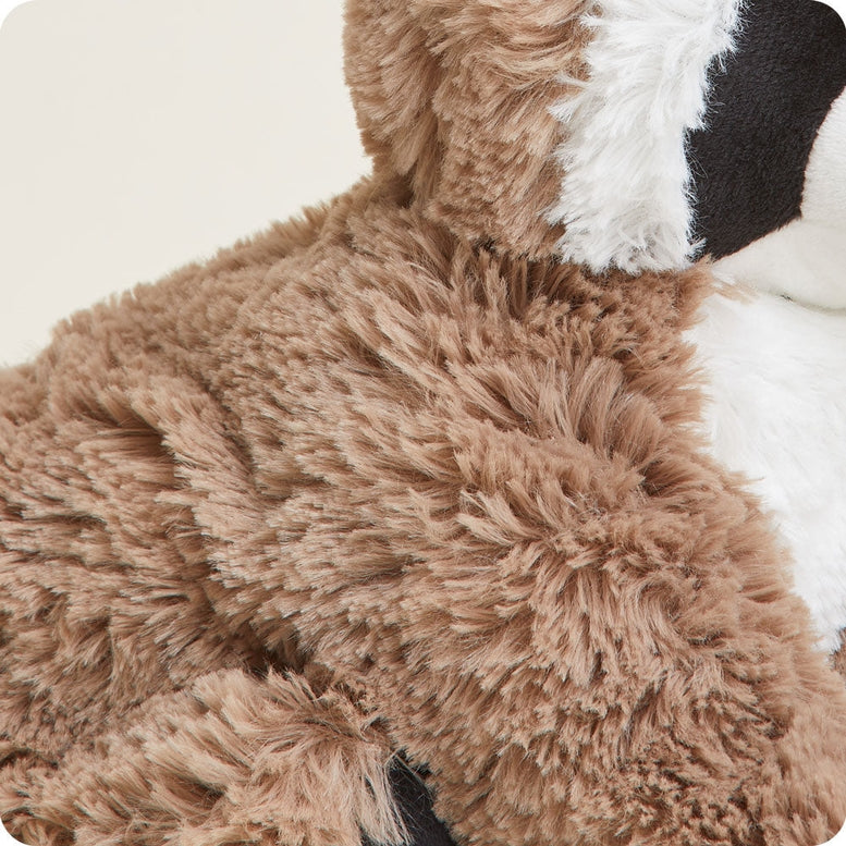 A close-up shot of the plush Raccoon by Warmies, highlighting its soft textured brown and white fur, black eye patches, and pointed ear.