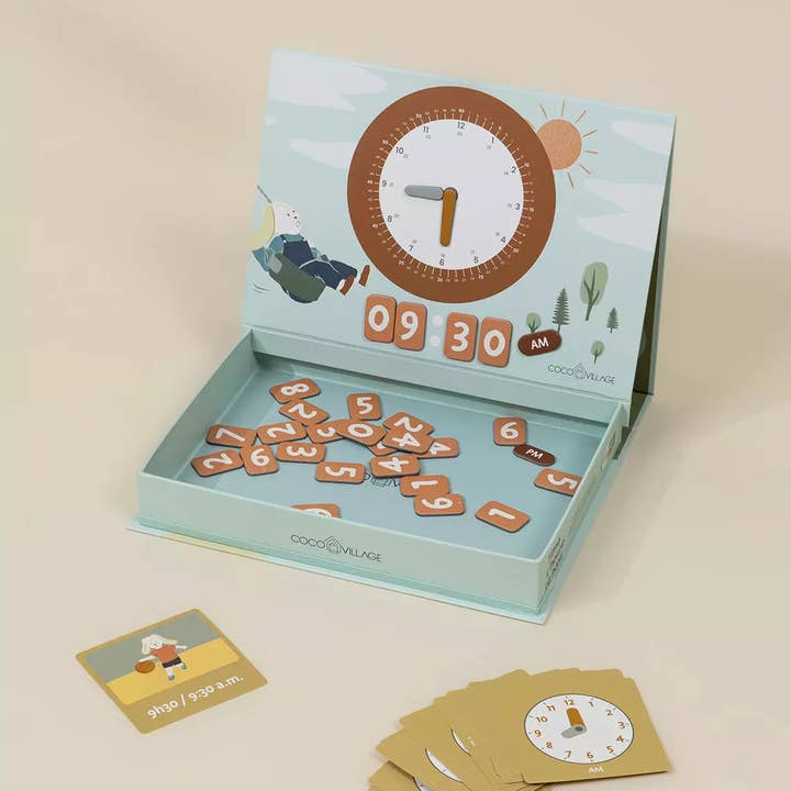 An open children's learning box with a light blue exterior and illustrated lid, showing wooden number tiles inside. A small instruction card and a stack of matching cards are placed in front on a warm beige background.