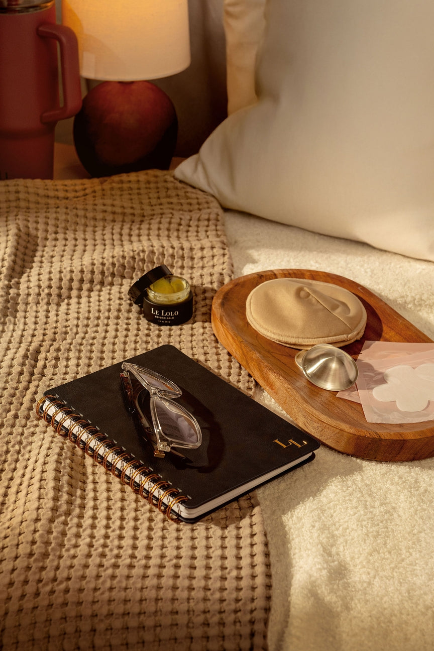 Personal care items on a wooden tray with a notebook on a bed.