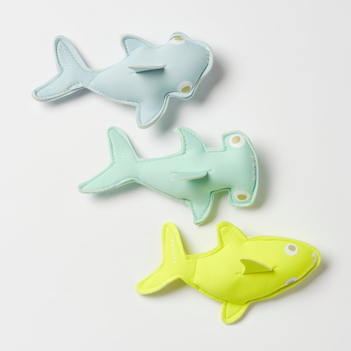 Three shark-shaped toys in light blue, green, and yellow on a white background