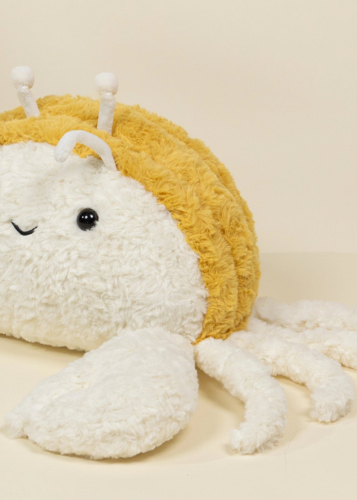 Plush snail toy with a yellow shell on a beige background