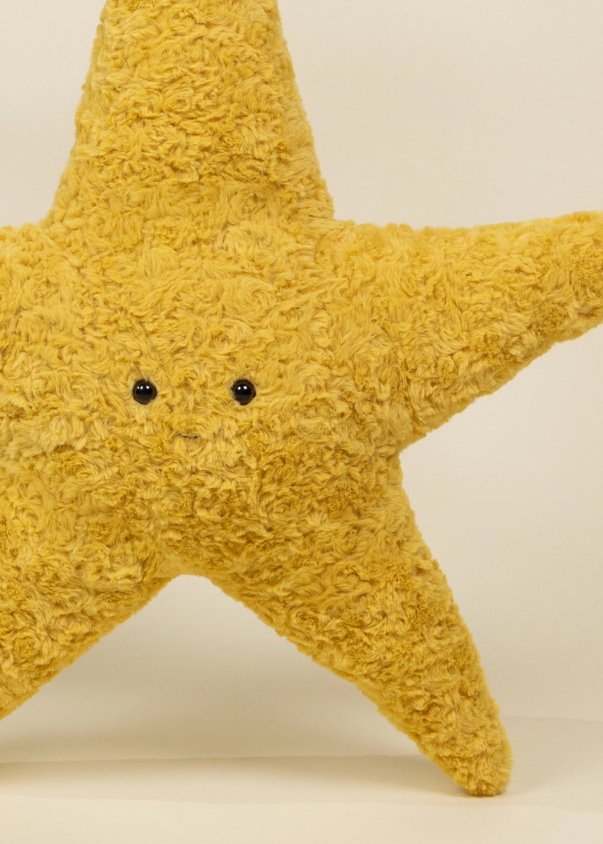Yellow star-shaped plush toy with black eyes on a beige background
