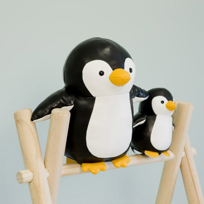 Two penguin toys sitting on a small wooden stool against a light gray background