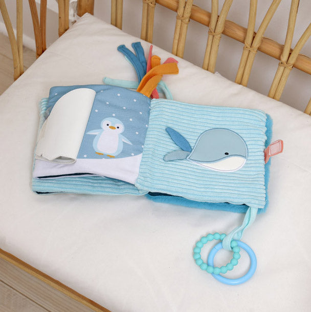 Baby soft book with penguin illustration and teething ring on a crib