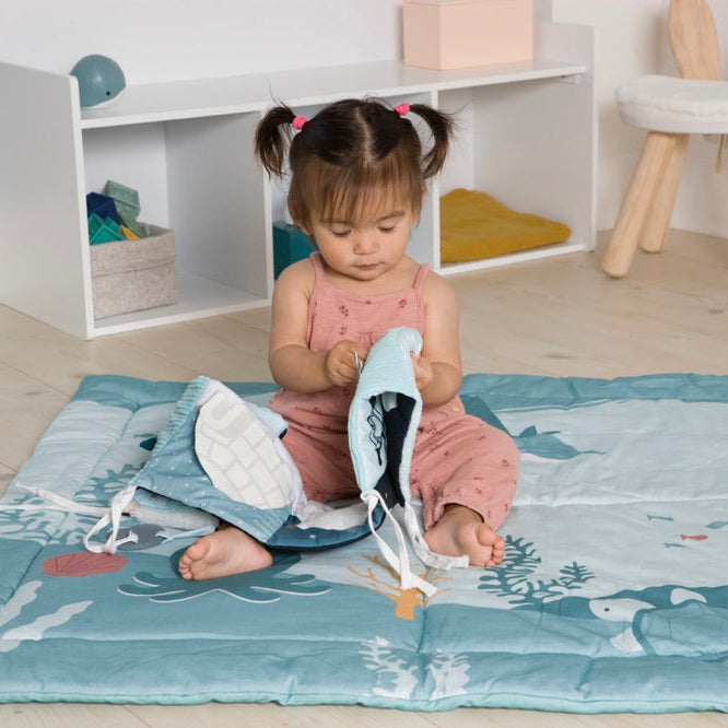 Child playing with toys on a mat in a room with shelves and toys.