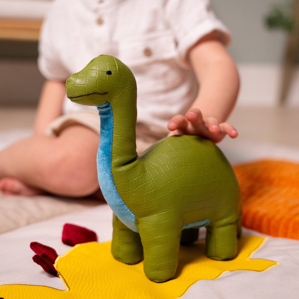 Child playing with a green dinosaur toy on a colorful mat