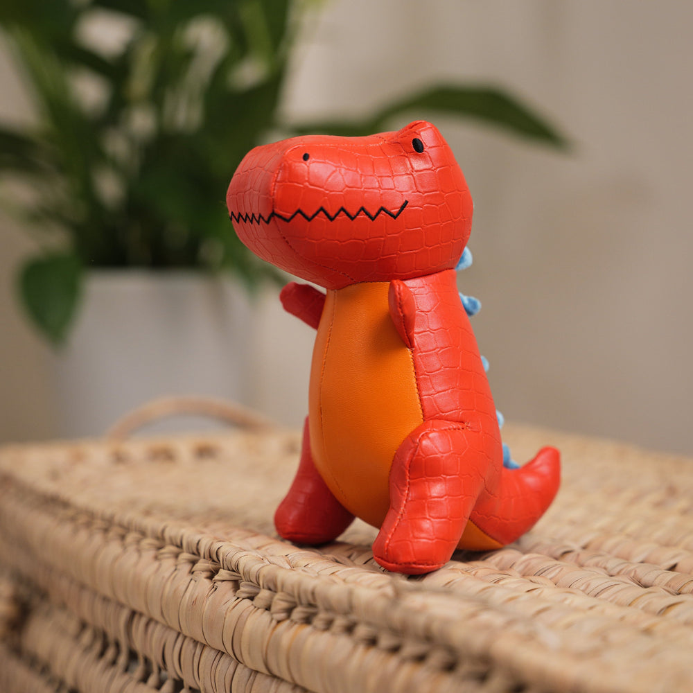 Red dinosaur toy on a woven surface with a blurred plant in the background