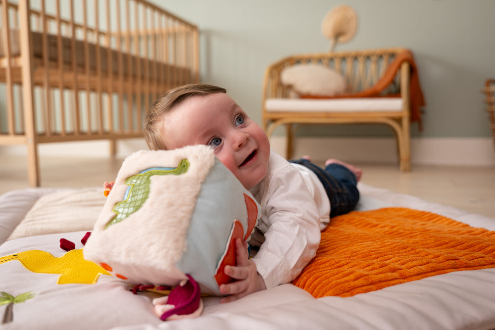Baby lying on a bed holding a plush toy in a nursery setting