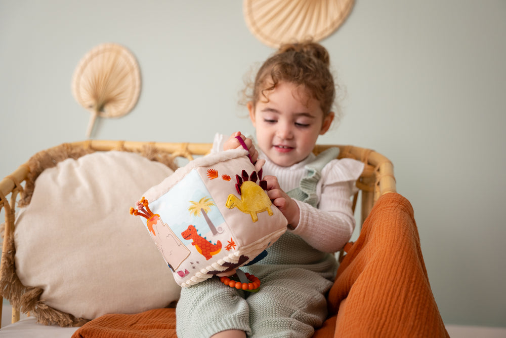 Child sitting on a couch holding a soft book with animal illustrations.