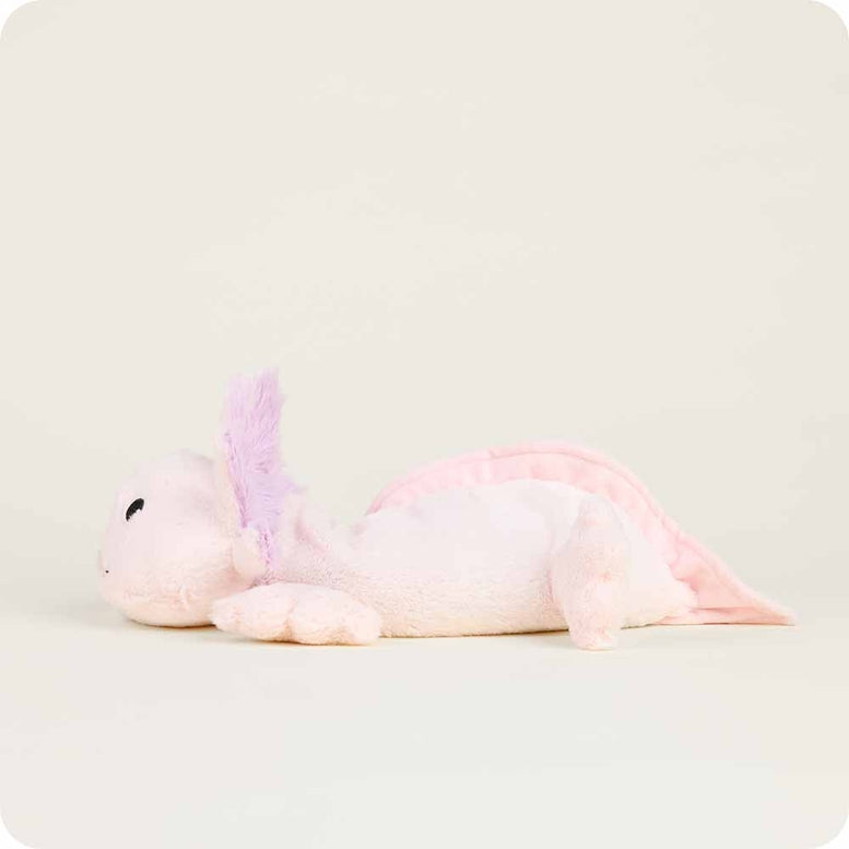 A side-profile view of the Pink Axolotl by Warmies plush toy resting on a neutral surface, showing its light pink body, stitched face, and purple feathery gills.