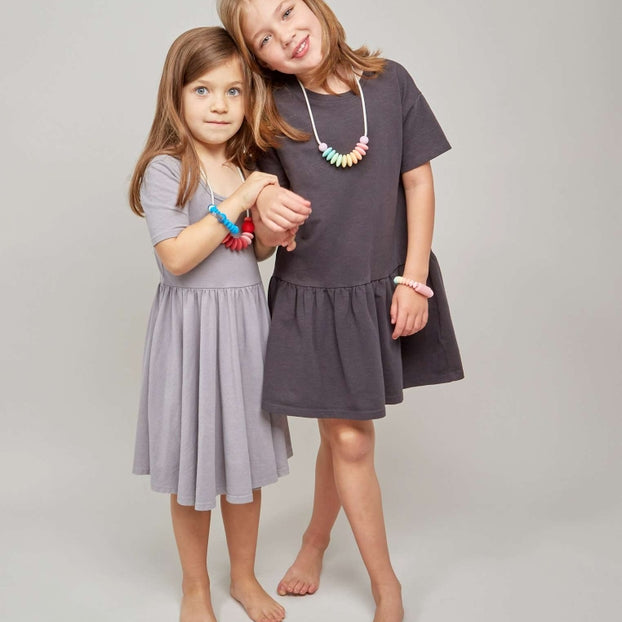 Two young girls wearing gray dresses standing against a plain background