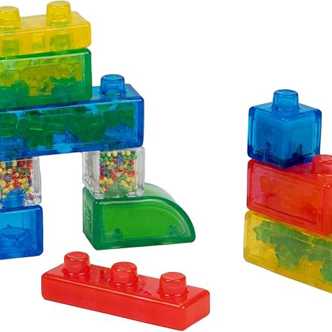 Two separate stacks of colorful, translucent Jelly Blox sensory blocks on a white background, featuring a mix of clear blocks filled with colorful beads and solid-colored blocks in blue, green, yellow, and red.